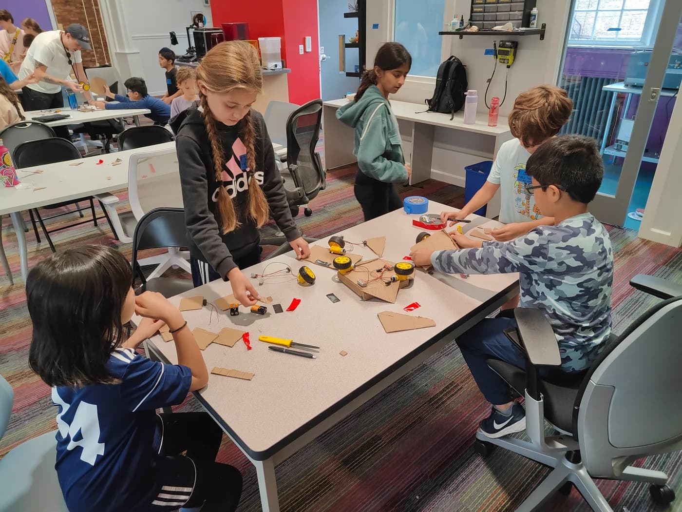 Students assembling cardboard robots around a workshop table