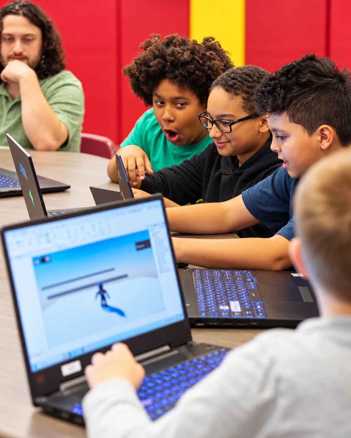 Young learners excitedly collaborating on laptops during a game-design activity