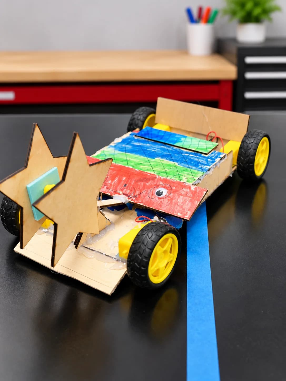 A colorful handmade robot with yellow wheels and a wooden star on its front